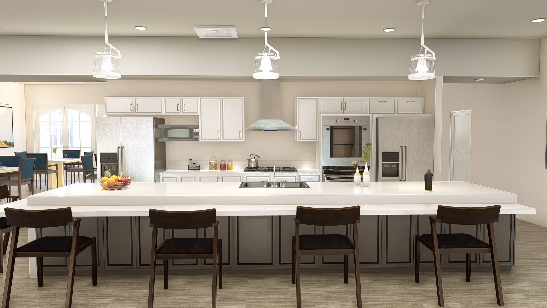 Modern kitchen with a large white island countertop featuring four dark wooden chairs. The kitchen has white cabinets, a stainless steel refrigerator, microwave, oven, and a range hood. There are pendant lights hanging from the ceiling and a bowl of fruit on the island. In the background, there is a dining area with tables and chairs near glass doors.