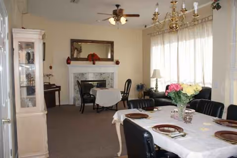 Well-lit senior living common area with a dining table, chairs, sofa, and fireplace.