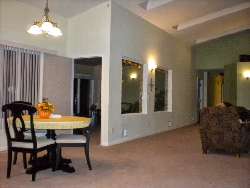 Open interior with a round dining table and chairs, a seating area with an armchair, and high ceilings with wall sconces.