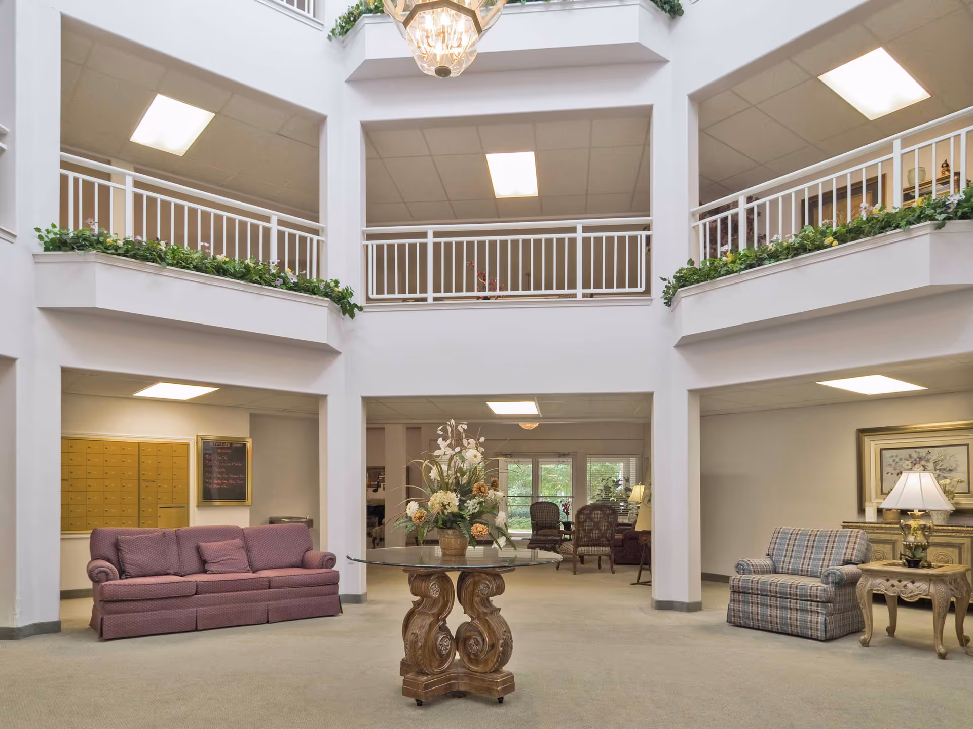Atrium-style lobby with seating, a central glass-top table holding a floral arrangement, and second-floor balconies.