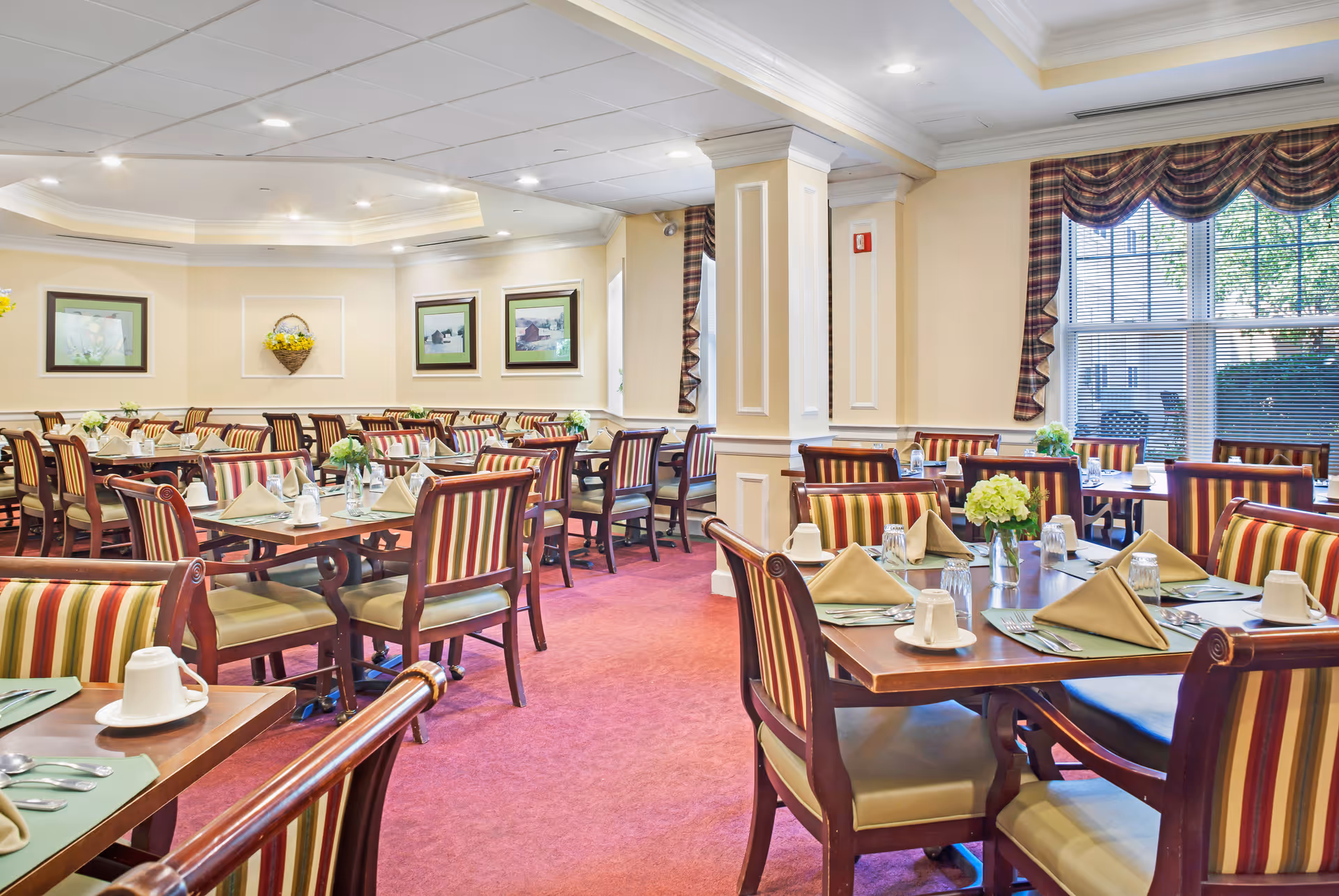 Spacious dining room with multiple set tables, striped chairs, folded napkins and floral centerpieces.