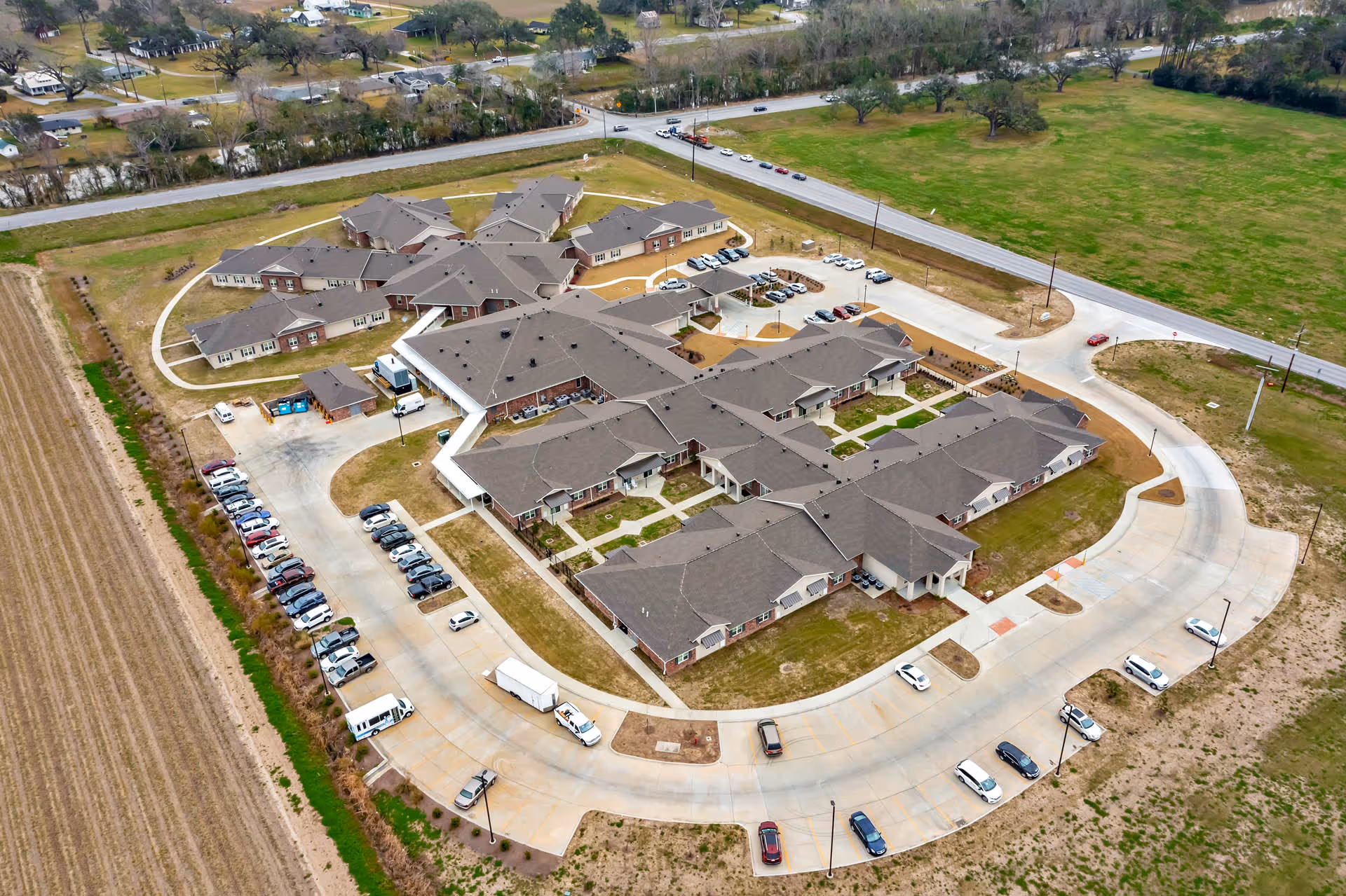 Aerial view of Thibodaux Healthcare and Rehabilitation Center showing multiple connected buildings with dark roofs, surrounded by parking lots with several cars and green fields around the facility.