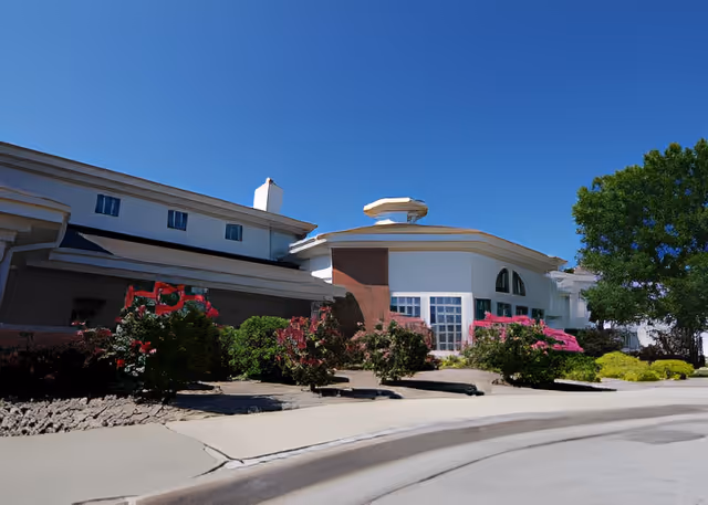 Front exterior of a senior living building with landscaped entrance, driveway, and clear blue sky.