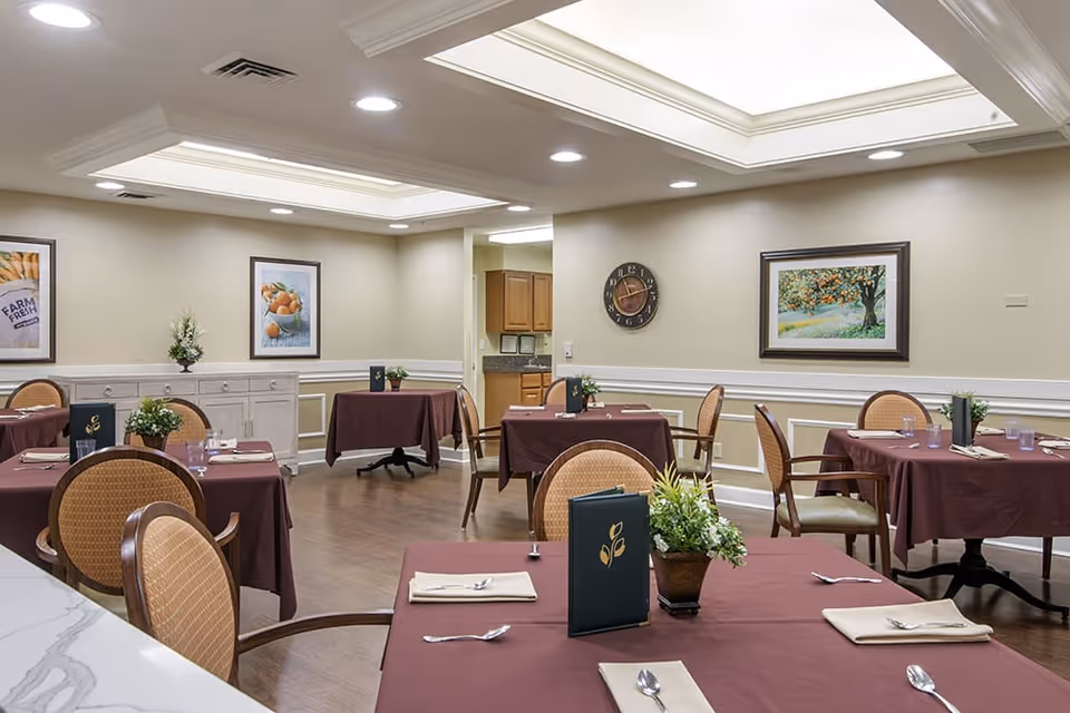 Dining room with tables set with burgundy tablecloths, chairs, framed artwork, and skylights in the ceiling.