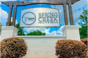 Outdoor entrance sign reading "Spring Creek Health & Rehab" mounted between white brick pillars with shrubs and a blue sky background.