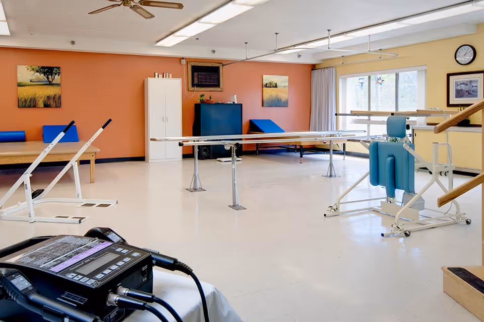 Bright rehabilitation room with parallel bars, therapy equipment, and exercise machines.