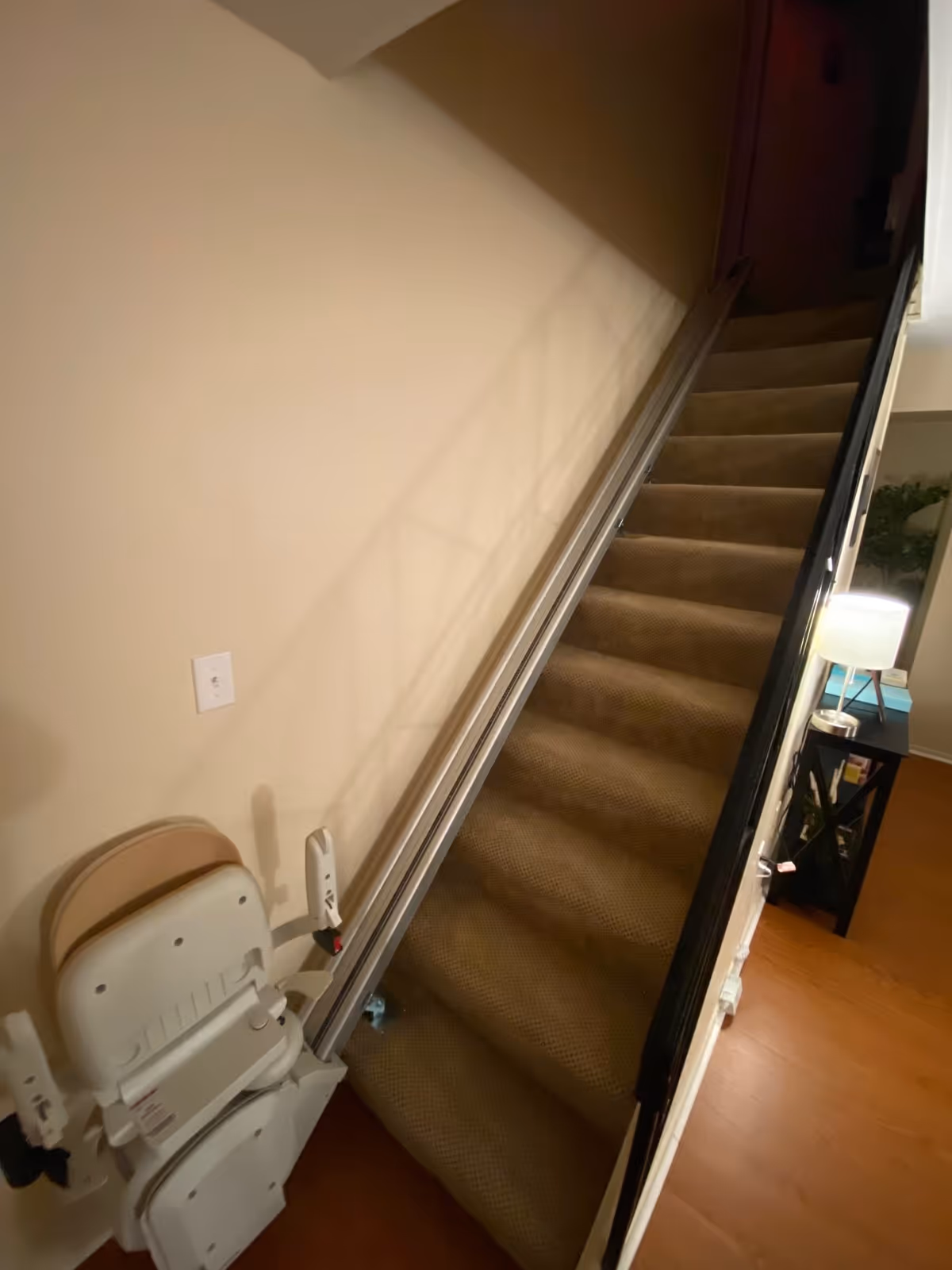 Interior view of a carpeted staircase with a stairlift chair and rail mounted along the wall.