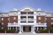 Front exterior view of Marwood Senior Apartments, a multi-story building with a combination of brick and light-colored siding, featuring balconies and a covered entrance supported by columns.