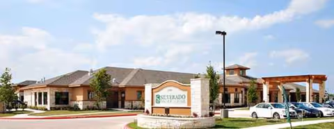 Exterior view of The Auberge at Onion Creek senior living facility with landscaping and parked cars.