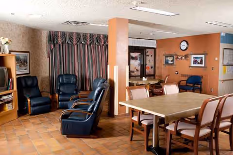 Common lounge and dining area with recliners, a wooden table, and wall clock.