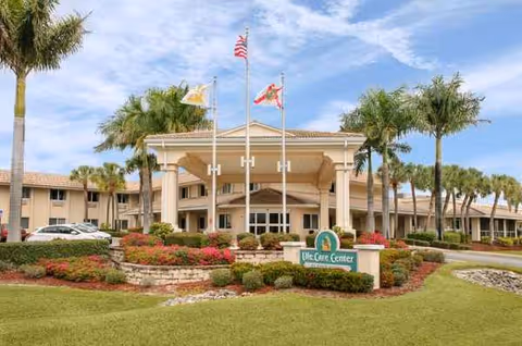 Entrance of Life Care Center of Punta Gorda with flags, palm trees, and landscaping.