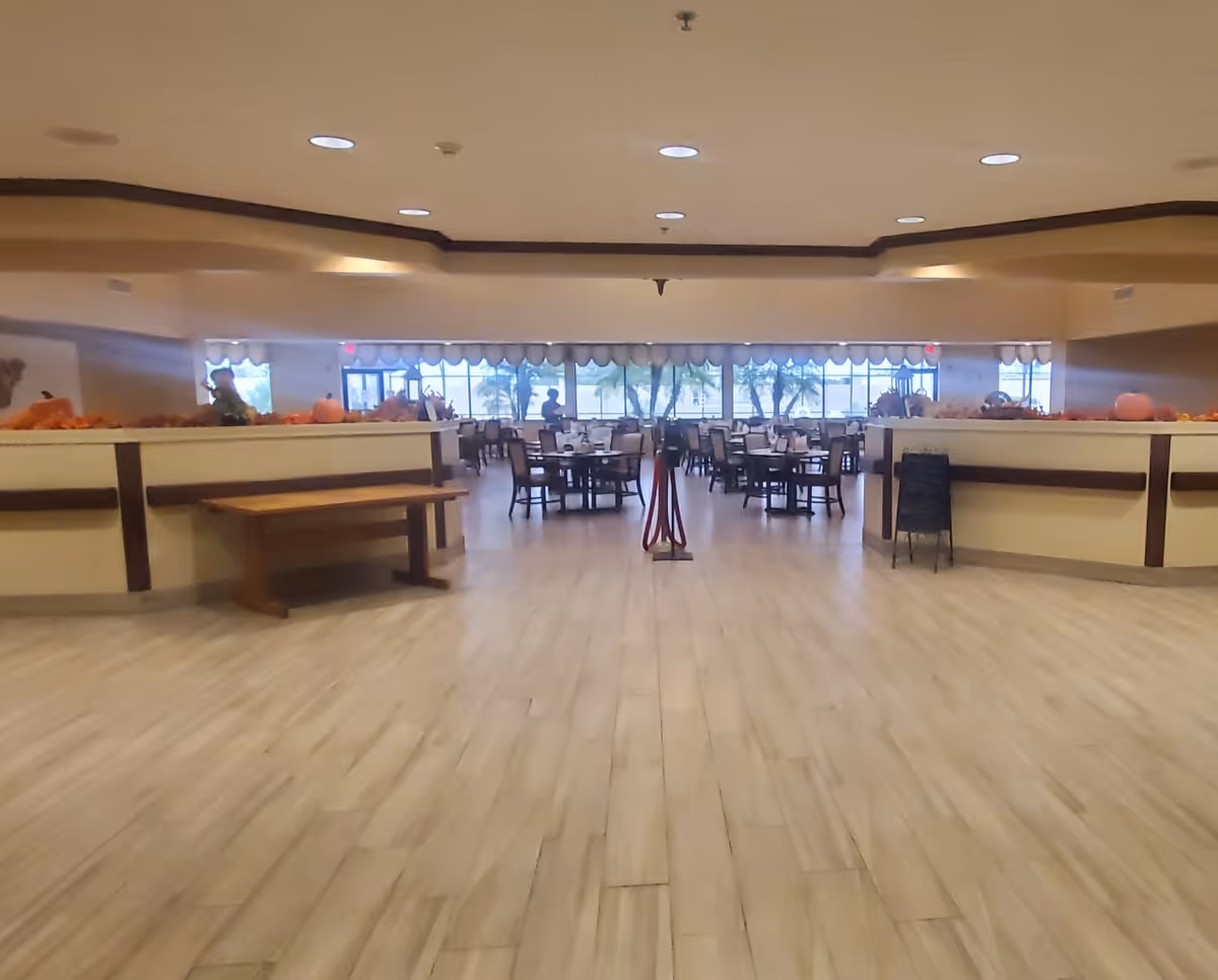 Spacious dining area with tables and chairs beyond a low partition and large windows along the back wall.