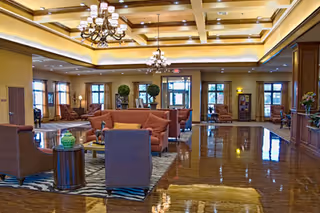 Spacious, well-lit senior living facility lobby with seating areas, chandeliers, and polished floors.