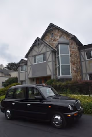 A black taxi parked in front of a Tudor-style multi-story building with stone and stucco exterior.