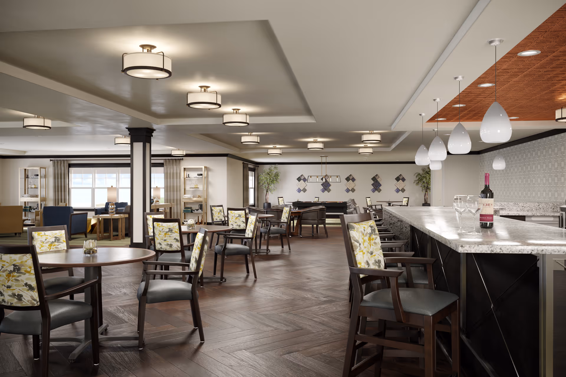 A spacious and well-lit common area in a senior living facility featuring multiple round tables with chairs that have floral patterned backs. There is a long marble countertop bar with high chairs on the right side, with a bottle of wine and wine glasses on the counter. The room has modern ceiling lights and large windows with curtains, and in the background, there is a seating area with armchairs and a pool table.