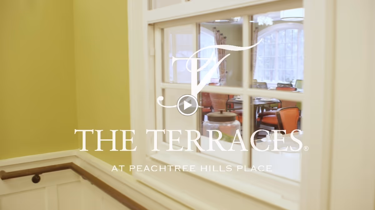 Interior hallway with a window looking into a dining area and a large "THE TERRACES AT PEACHTREE HILLS PLACE" logo overlay.