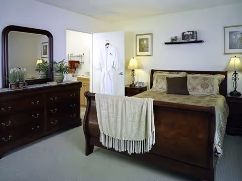 Cozy bedroom featuring a dark wood sleigh bed with a throw blanket, matching dresser and nightstands with lamps, and an open door with a hanging robe.