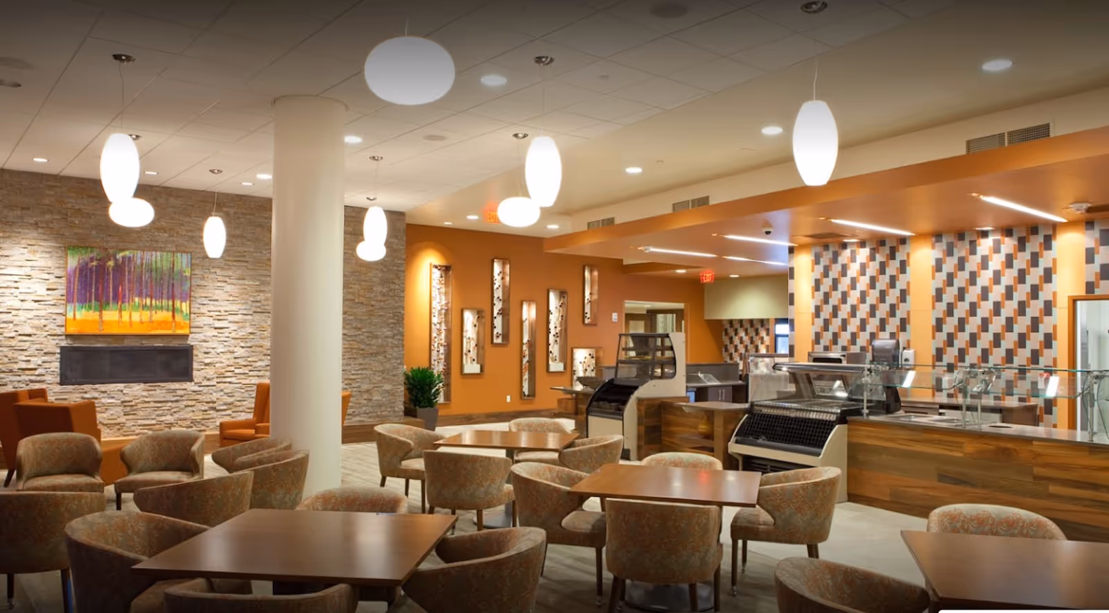 Bright modern dining and lounge area with multiple tables and upholstered chairs, a service counter, pendant lighting, and warm decorative accents.