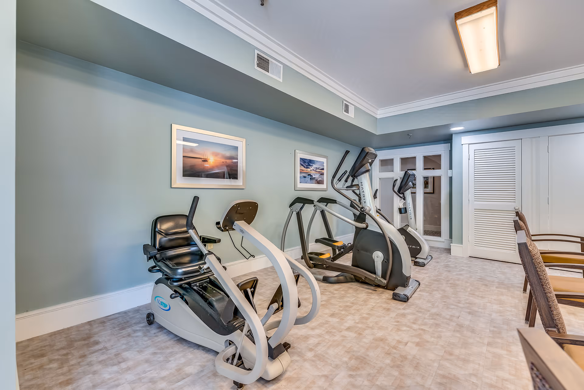 Small fitness room in a senior living residence with a recumbent bike and two elliptical machines against a mint-green wall.