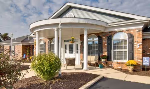 Exterior entrance of a brick senior living facility with curved portico and seating.