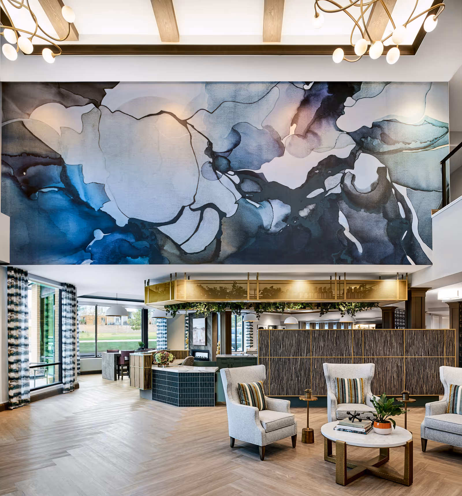 Spacious modern senior living lobby with armchairs around a coffee table, a large abstract mural on the upper wall, and floor-to-ceiling windows.