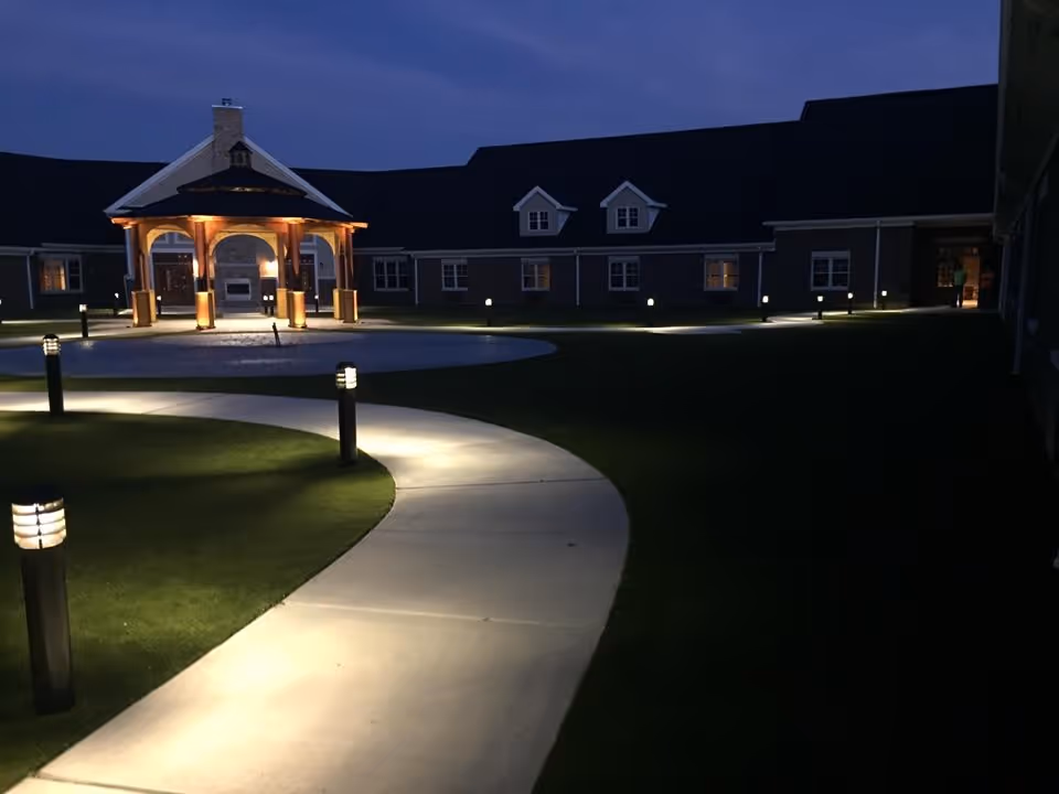 Lit curved walkway at night leading to a gazebo in the courtyard of an assisted living facility.