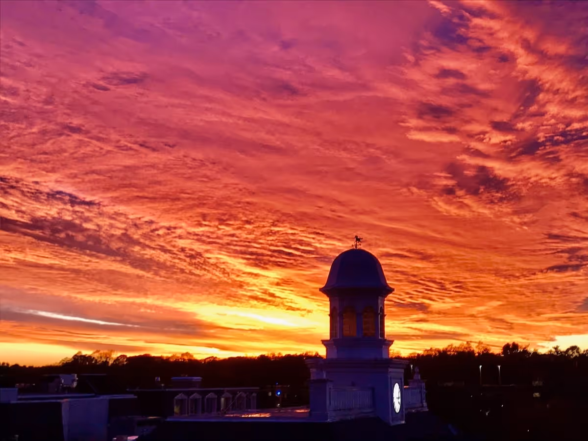 A dramatic sunset sky with vibrant orange, pink, and purple clouds above a building with a clock tower silhouette.