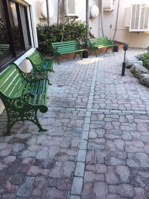 Small paved courtyard with three green metal benches along a building wall and exterior HVAC units.