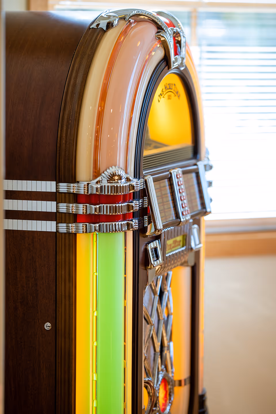 Close-up of a vintage illuminated jukebox with colorful neon panels and chrome details inside a room.