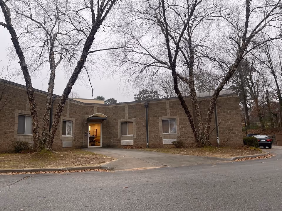 Single-story brick building with an entrance awning and leafless trees in front on an overcast day.