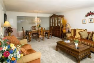 Spacious furnished living room with sofas, coffee table and an adjacent dining area with a chandelier and china cabinet.