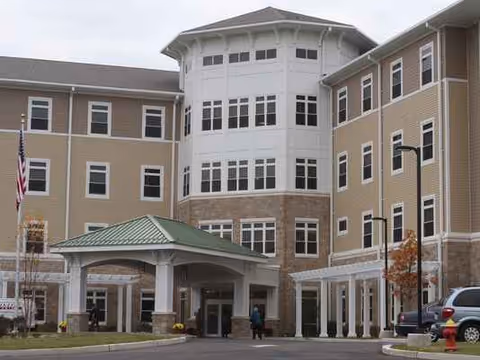 Exterior view of a multi-story beige senior living center with rounded central tower.