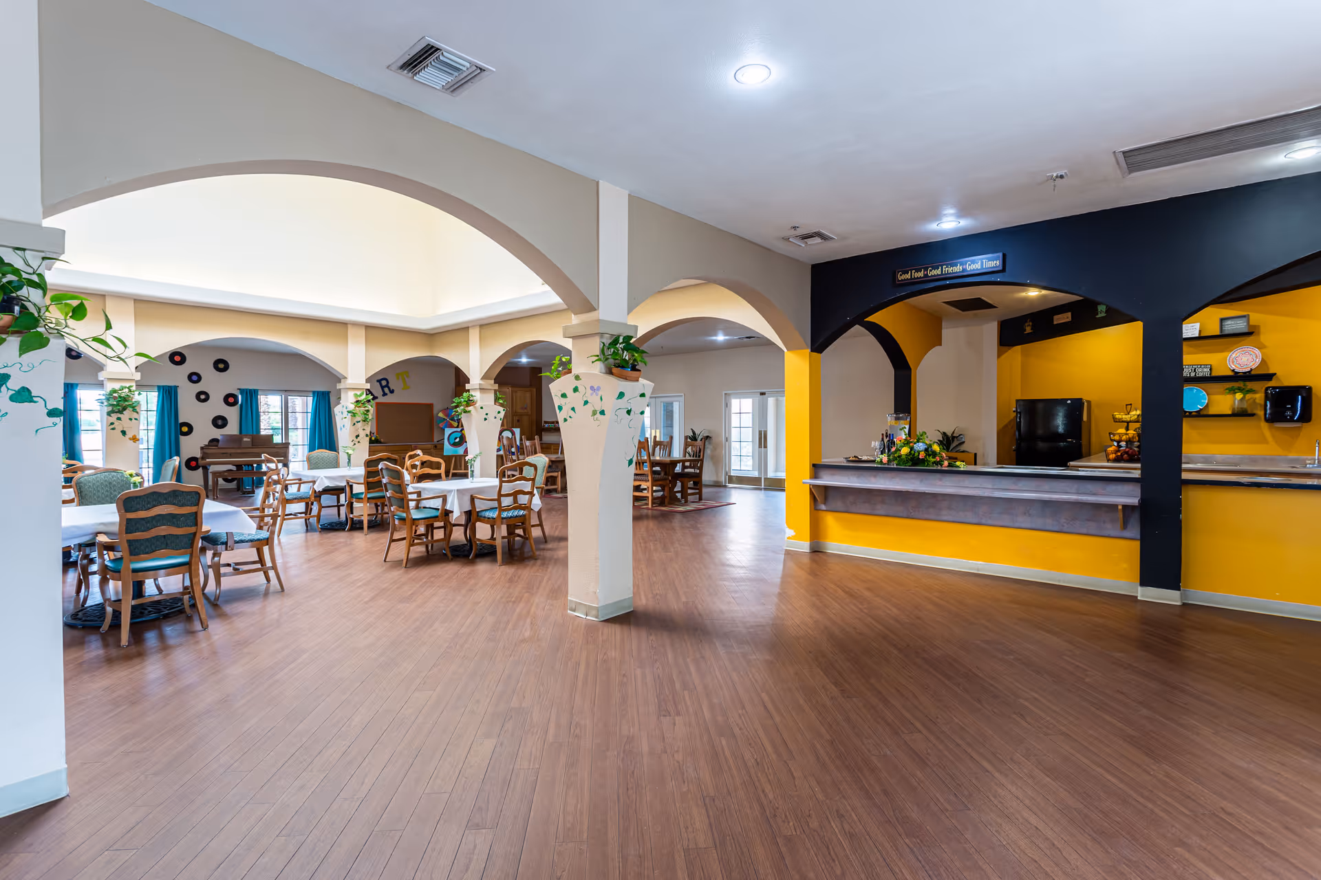 Spacious senior living dining and common area with tables, chairs, arched columns and a serving counter.