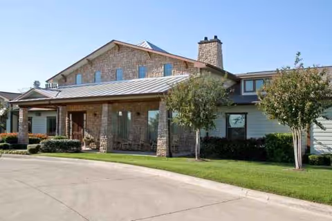 Stone-front assisted living facility entrance with covered walkway and neatly landscaped grounds.