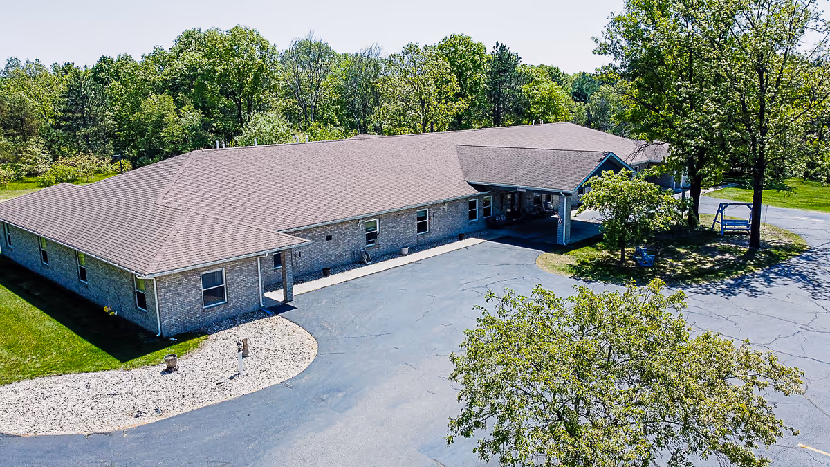 Aerial view of a single-story brick senior living building with a covered entrance, driveway and surrounding trees.
