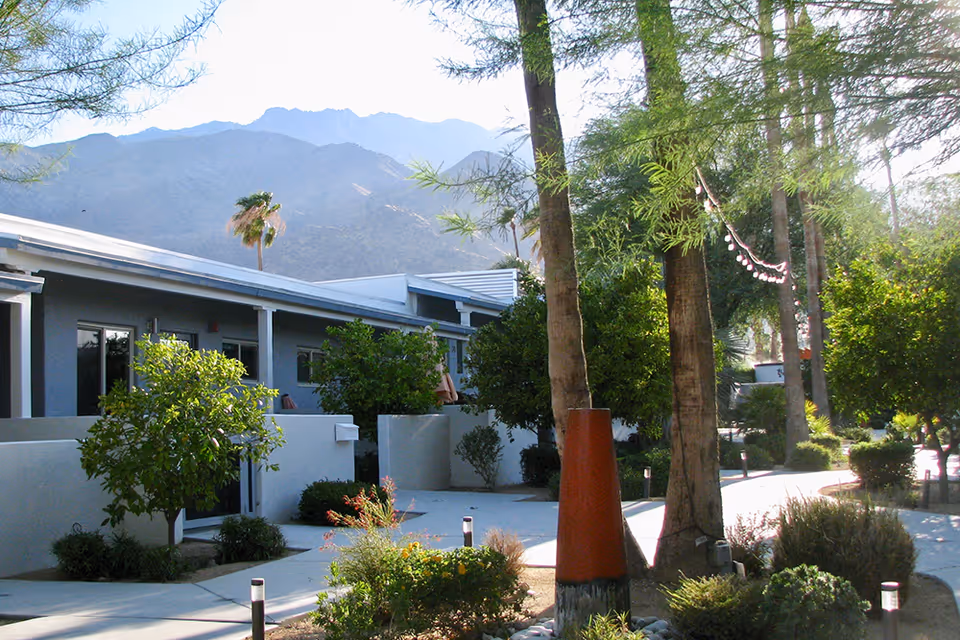 Single-story building with a tree-lined courtyard and walkways, set against distant mountains.