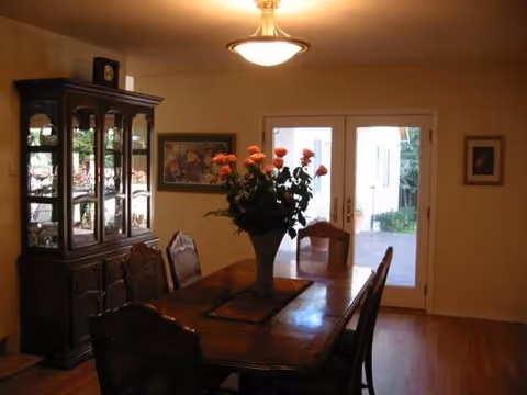 A dining room with a wooden table, chairs, a floral centerpiece, and a glass cabinet.