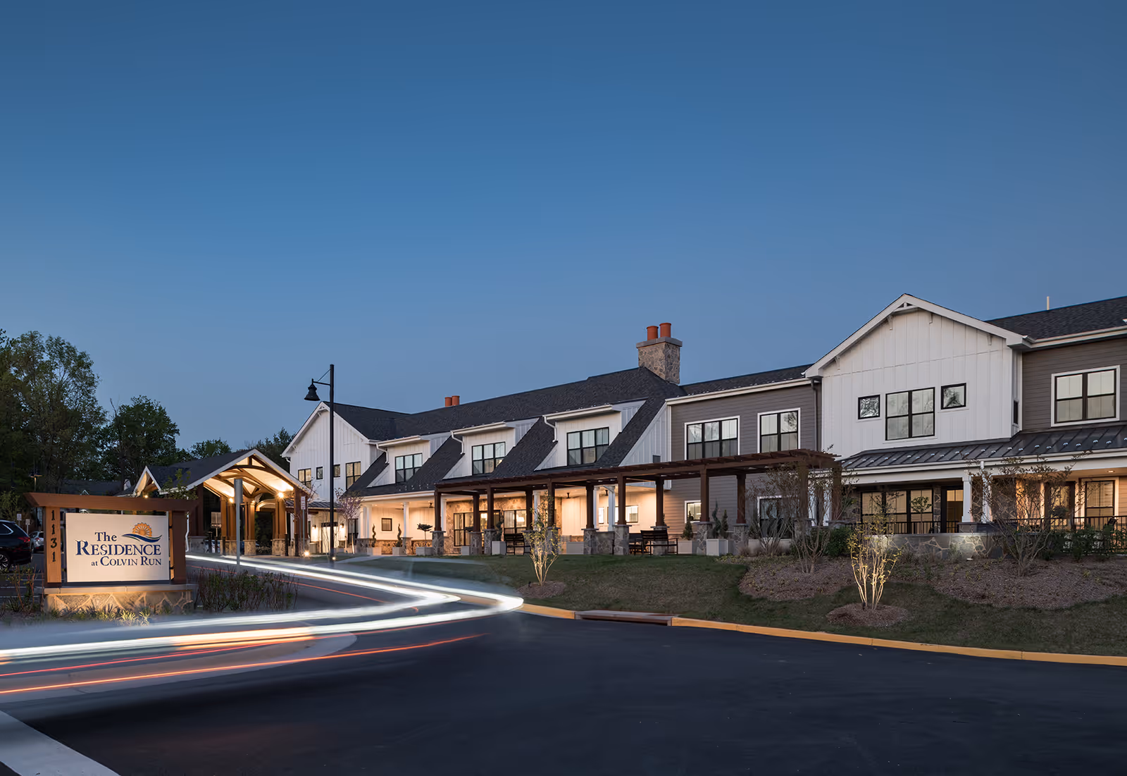 Dusk exterior view of The Residence at Colvin Run building with a lit entrance, pergola, and the facility sign in the foreground.