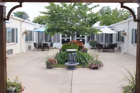 Outdoor courtyard with a central tree, fountain, planters, and seating between light buildings.
