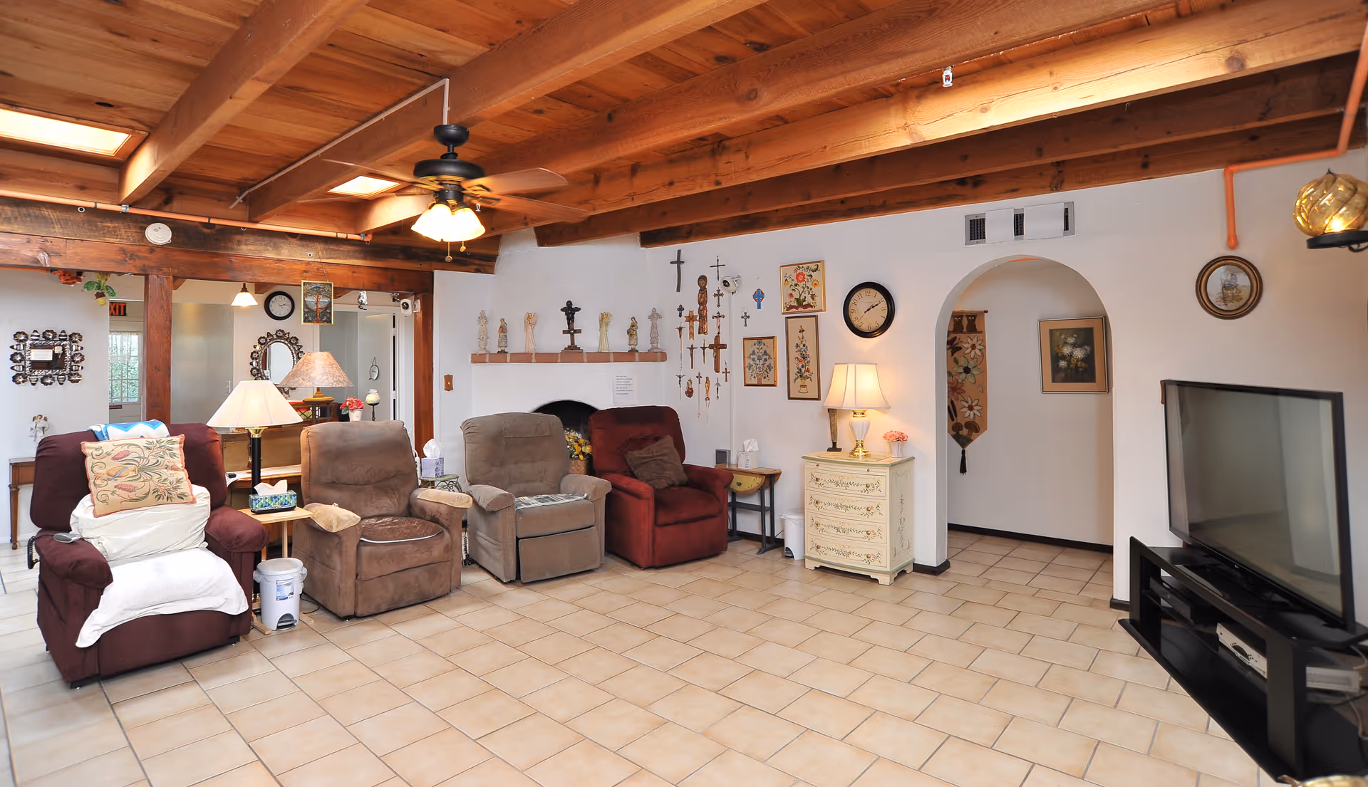 Common area living room with several recliner chairs under exposed wooden beams, wall décor and a flat-screen TV.