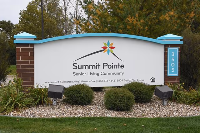 Outdoor sign for Summit Pointe Senior Living Community with landscaping including bushes and grass around the base, and trees in the background.