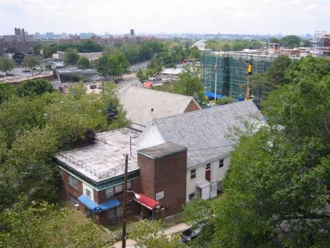 Aerial view of a small white building with brick chimney, storefront awning, amid trees and construction.