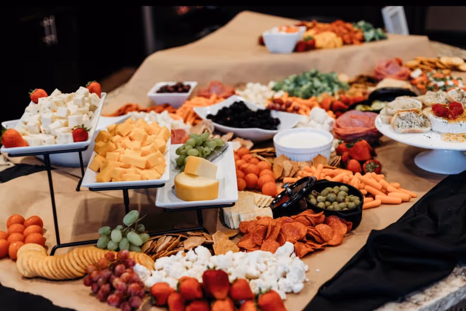 A catered charcuterie-style spread with cheeses, crackers, fruits, olives and other appetizers arranged on platters and boards.