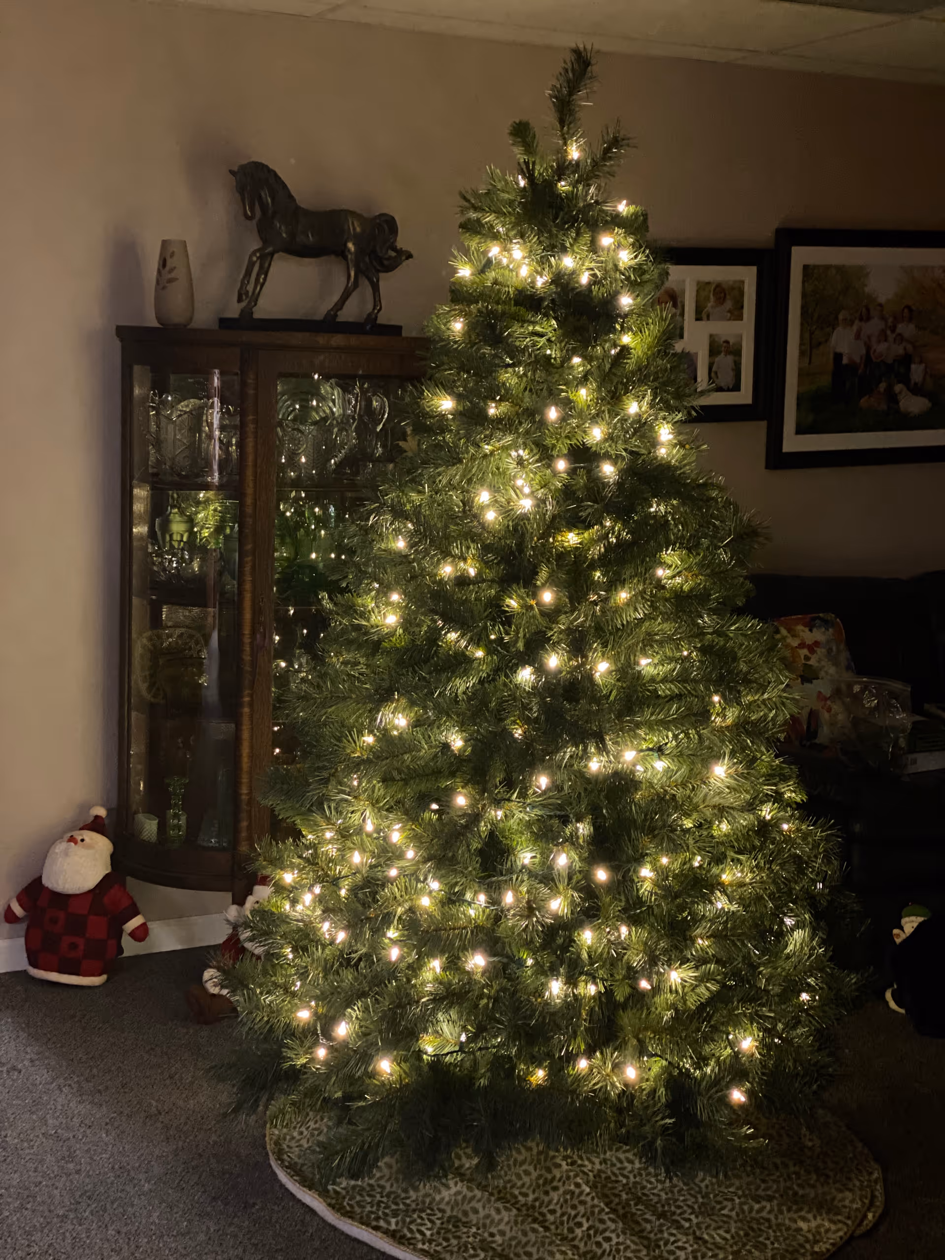 A lit Christmas tree in a living room next to a glass display cabinet and holiday decorations.