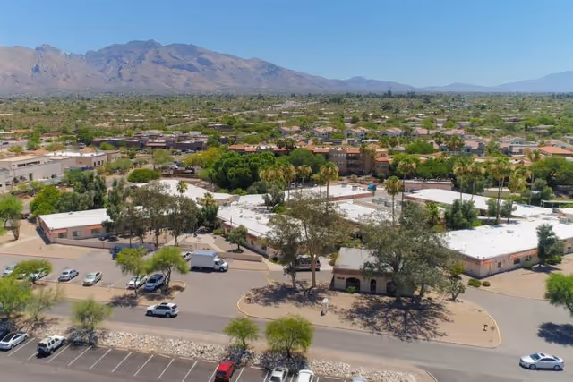 Aerial view of Casas Adobes Post Acute Rehabilitation Center surrounded by trees and parking lots, with a mountainous landscape in the background under a clear sky.