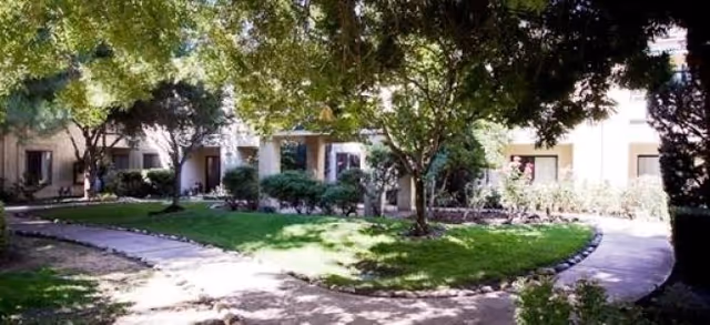 Exterior courtyard of Del Monte Assisted Living & Memory Care in Stockton, with trees and walkways.