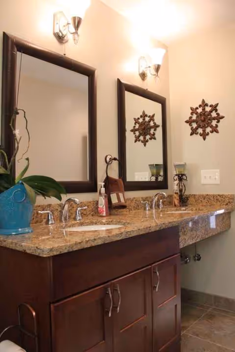 Double-sink bathroom vanity with granite countertop, two framed mirrors, and decorative accents.