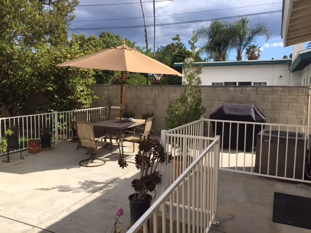 Outdoor patio with table, chairs, umbrella, and grill in a fenced courtyard