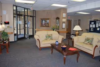 Lobby seating area with beige couches, coffee table, lamp, and framed art.