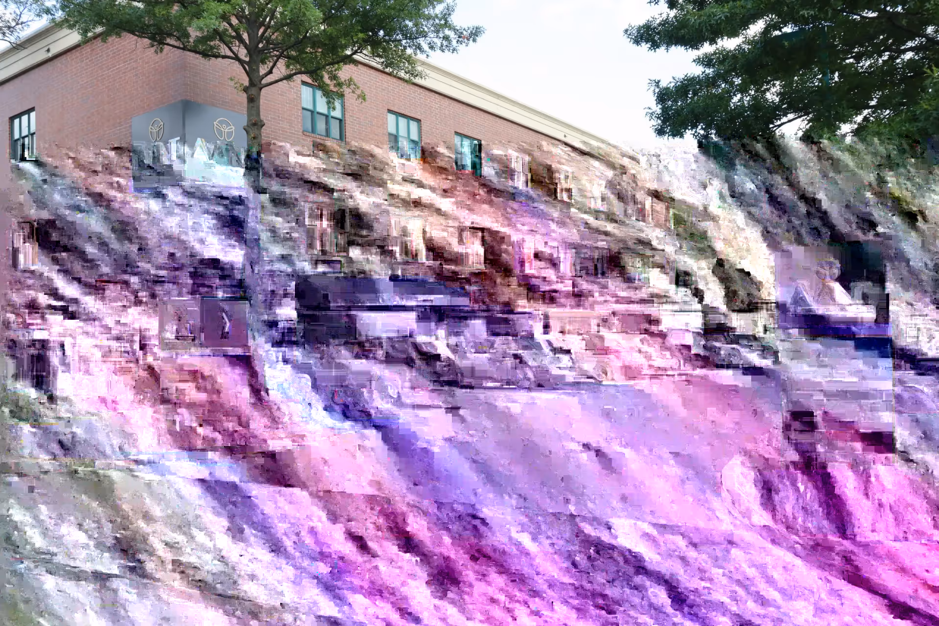 Exterior view of a brick senior living facility perched on a rocky hillside with trees.